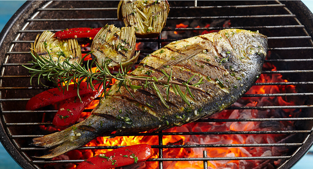 A whole grilled bream with artichokes on a coal-fired grill