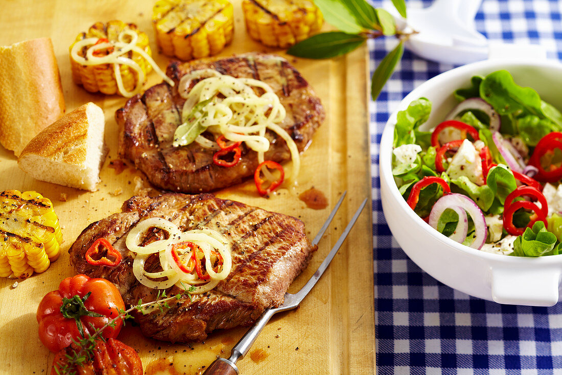 Grilled pork collar steaks in a beer marinade with grilled corn cobs and a colourful salad