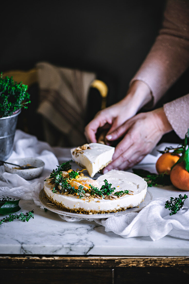 White creamy tasty tangerine cake decorated with green and citrus on table cutting by cook hands