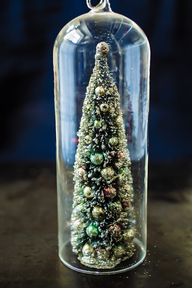A decorative Christmas tree under a glass cloche