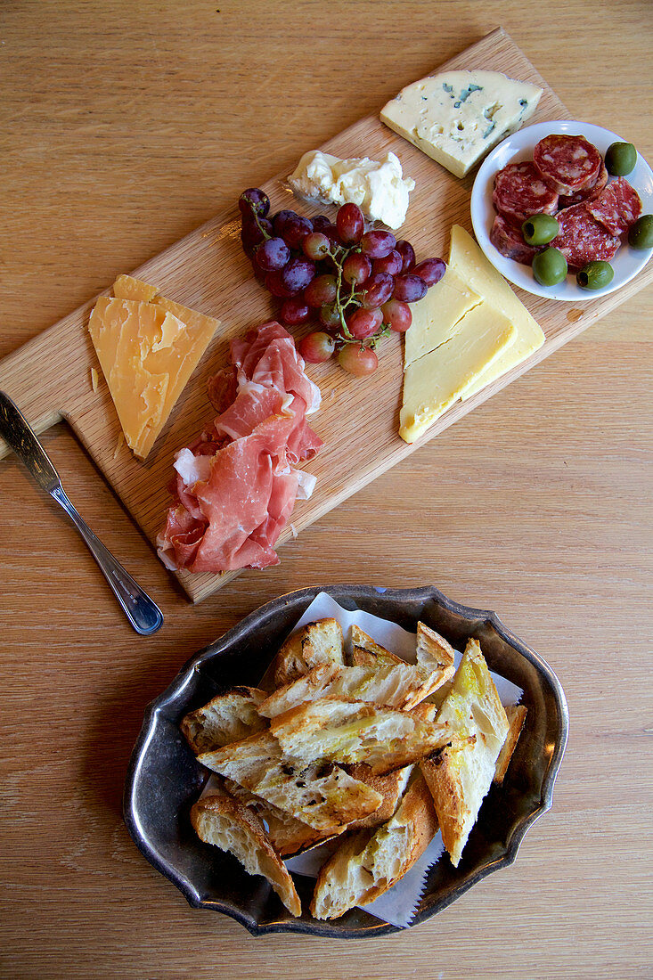 Käse, Schinken, Wurst und Trauben auf Holzbrett dazu Baguettebrot