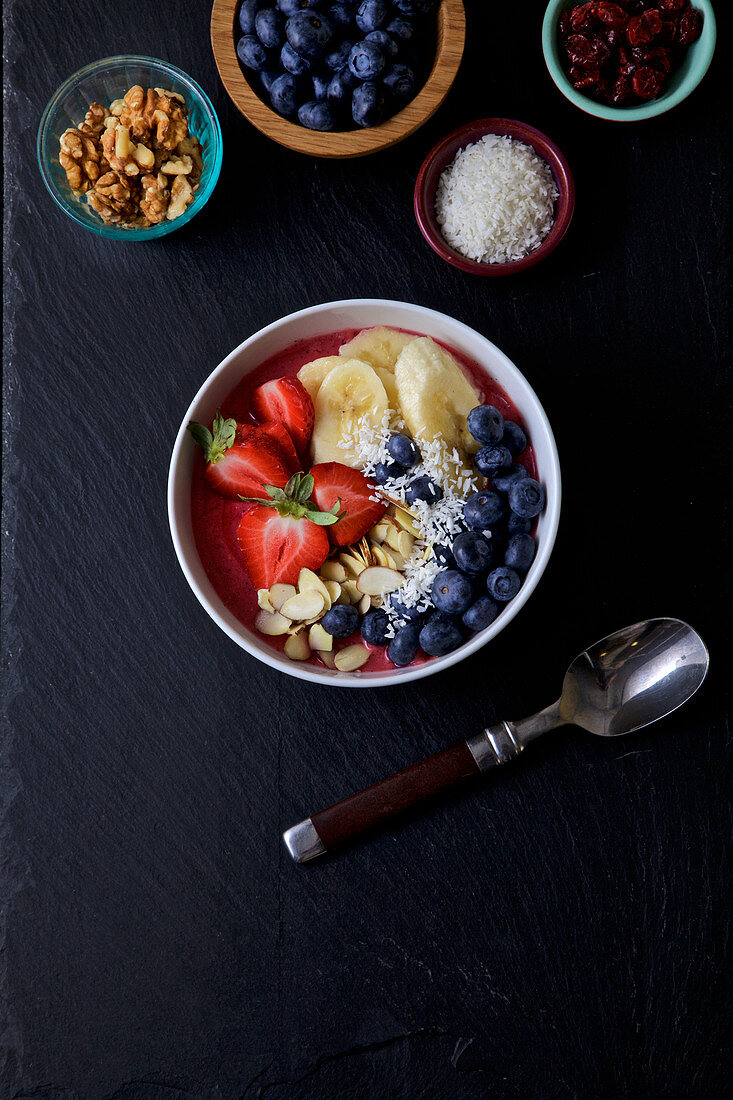 Pitaya bowl with bananas, blueberries almonds, strawberries, coconuts flakes and cranberries