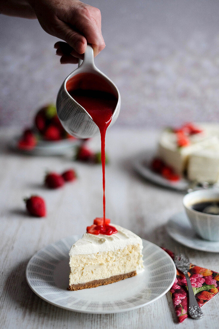 Strawberry sauce being poured over American cheesecake