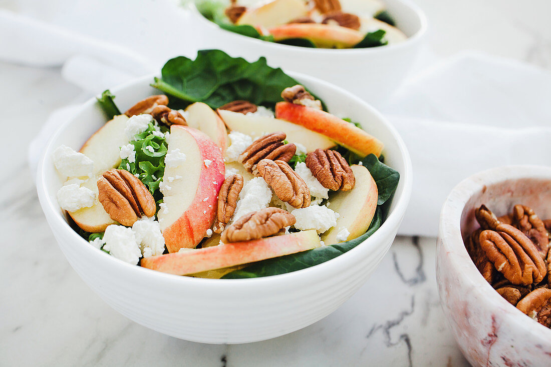 Served bowls with cut apple and pecan salad on table with apple and walnuts