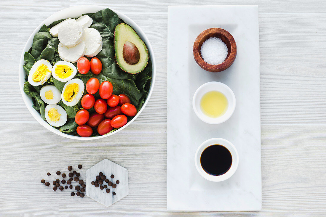 Served bowl of salad with spinach eggs avocados tomatoes and mozzarella cheese on table with condiments sauces
