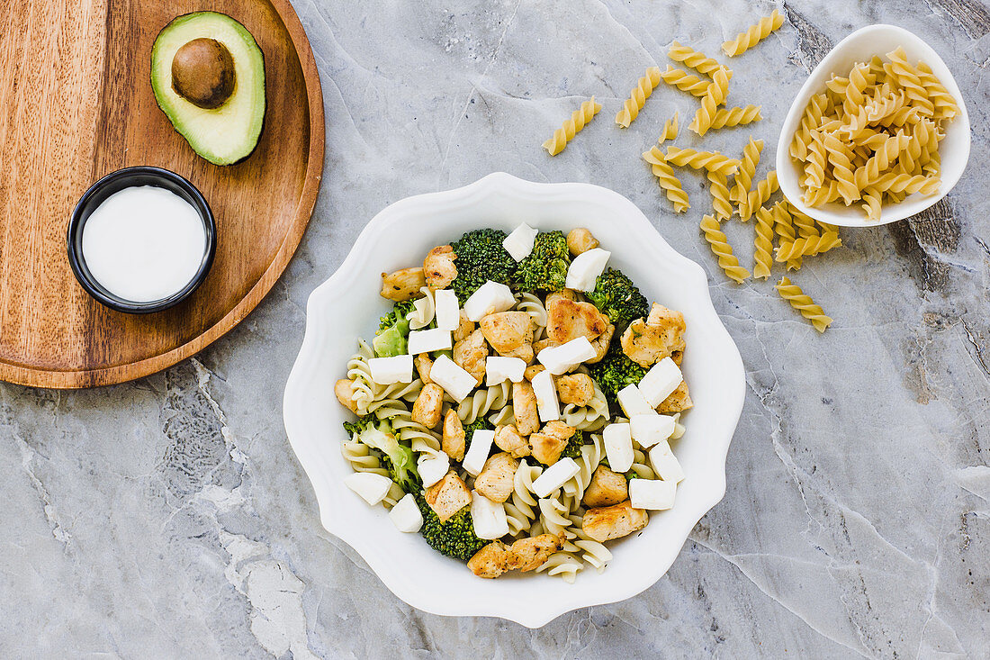 Served bowl of salad with chicken macaroni broccoli and cheese on table with avocado sauce and plate with macaroni