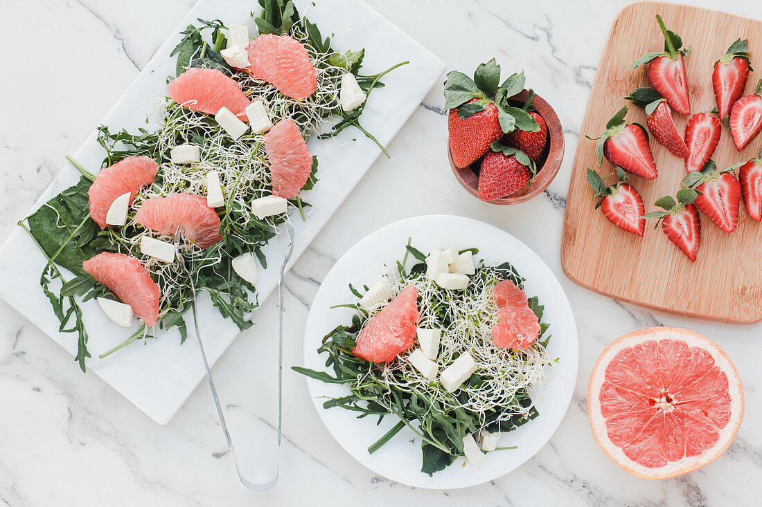 Top view of bowls with strawberry, grapefruit and rocket salad on table served on kitchen boards