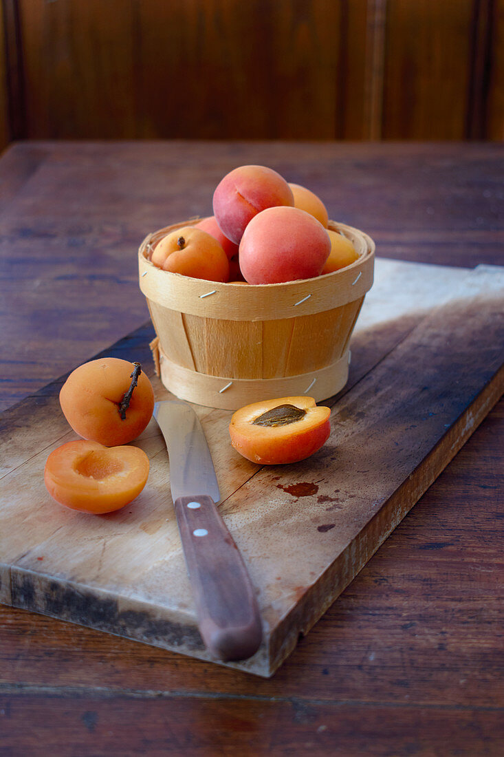 An arrangement of apricots in a wooden basket with a halved apricot next to it