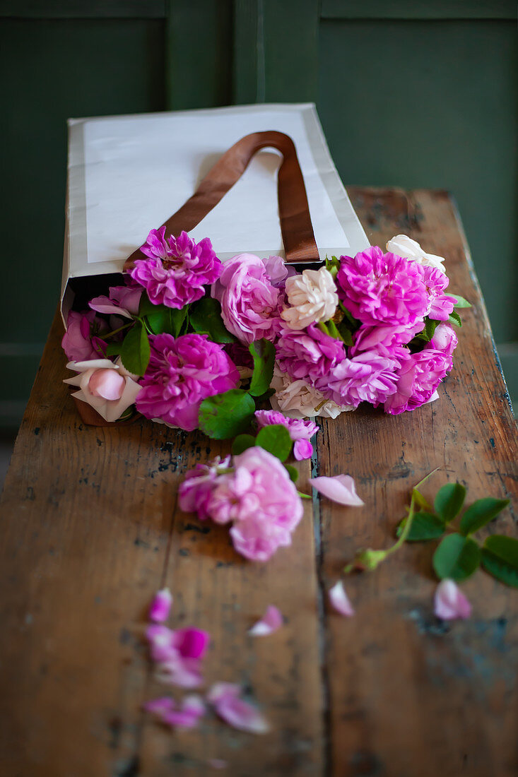 Pinkfarbene Rosen in Papiertüte auf Holztisch