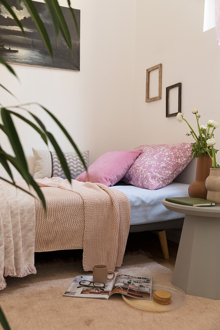 Pink pillows on sofa bed and grey side table in feminine apartment