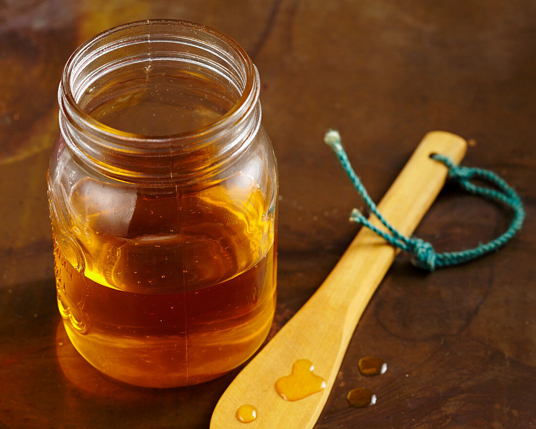 Honig im Glas und Honigtropfen auf Holzlöffel