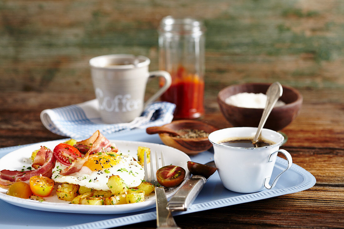 Bratkartoffeln, Speck, Spiegelei und Tomaten zum Frühstück, dazu Kaffee