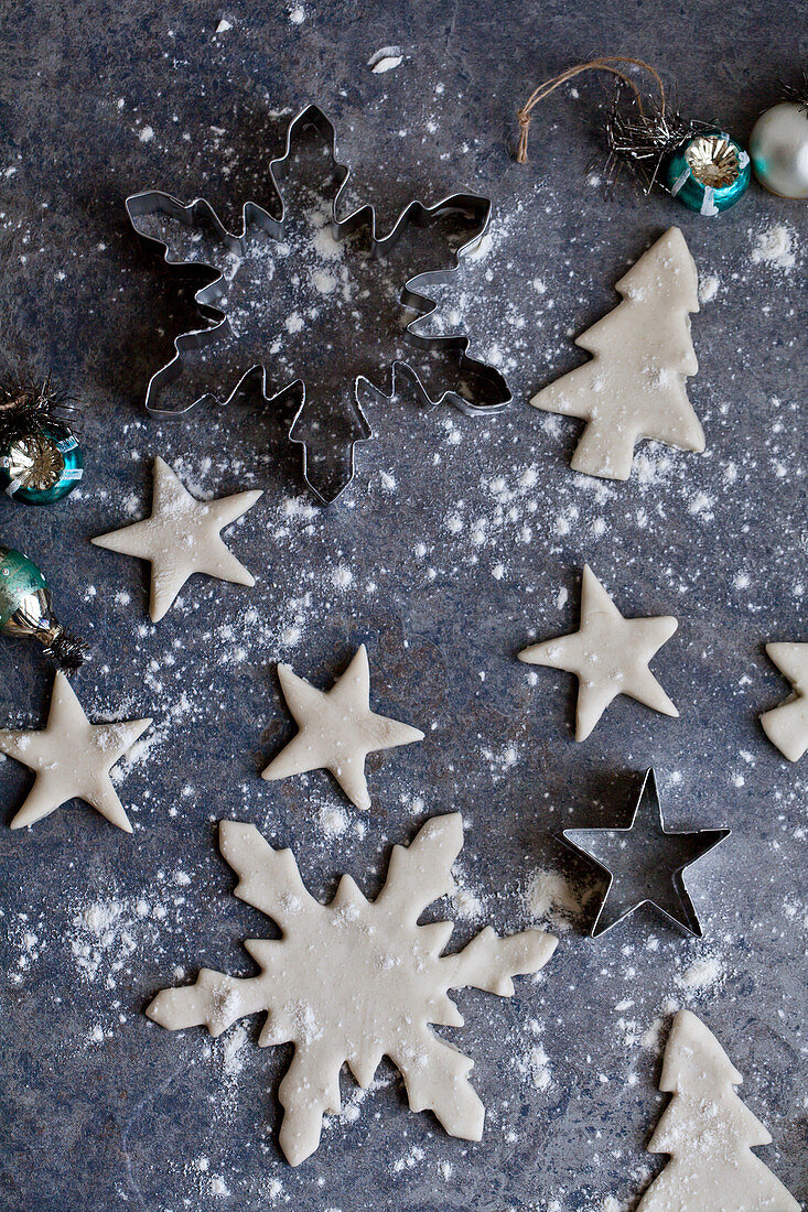 Holiday cookies being made and dusted with flour - with snowflake and star cookie cutters and ornaments sitting beside