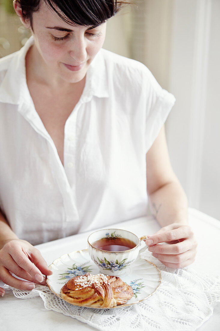 Frau am Tisch mit Tasse schwarzem Tee und Plunderteilchen