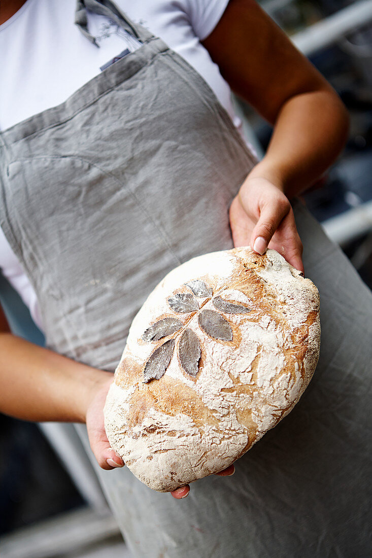 Female baker holding fresh bread with leaf pattern