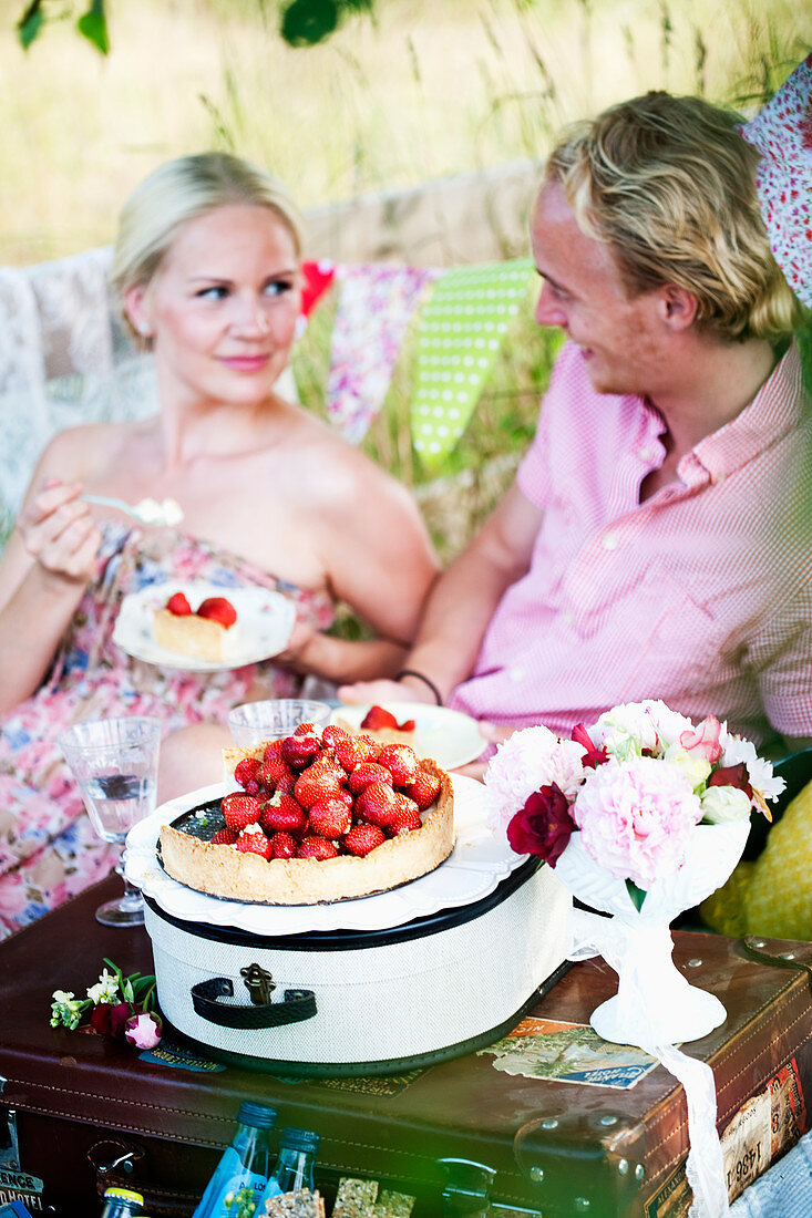 A couple eating strawberry tarts at a picnic