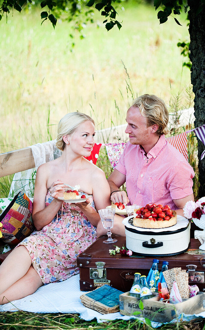 A couple eating strawberry tarts at a picnic