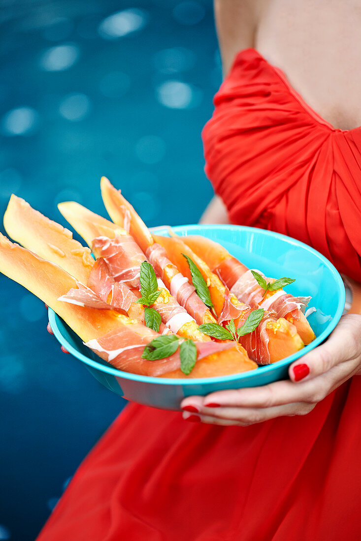 Frau hält Melone mit Schinken in Schüssel