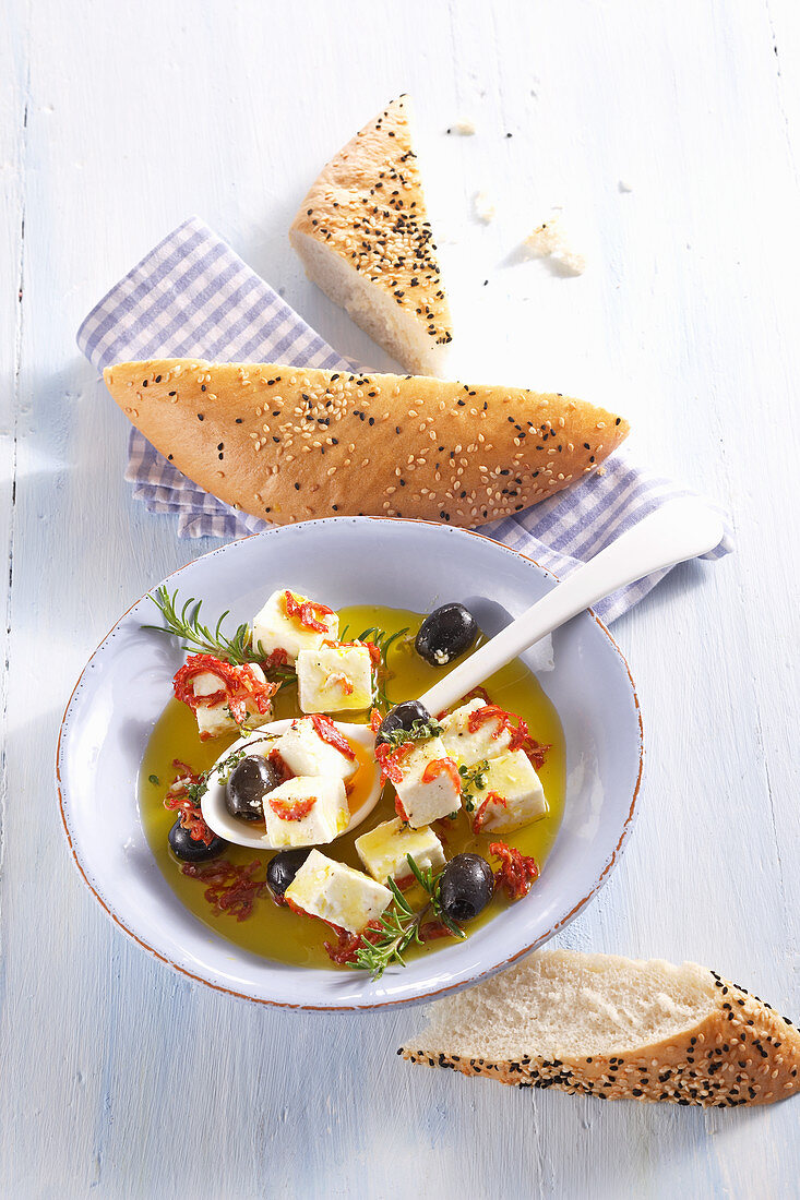 In Olivenöl eingelegter Schafskäse mit Oliven, Rosmarin, Fladenbrot, getrockneten Tomaten und Thymian