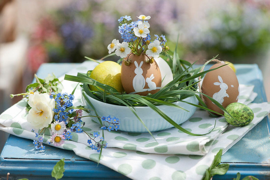 Easter nest with painted Easter eggs, bouquets of forget-me-nots, strawberry blossoms, primrose, and daisies