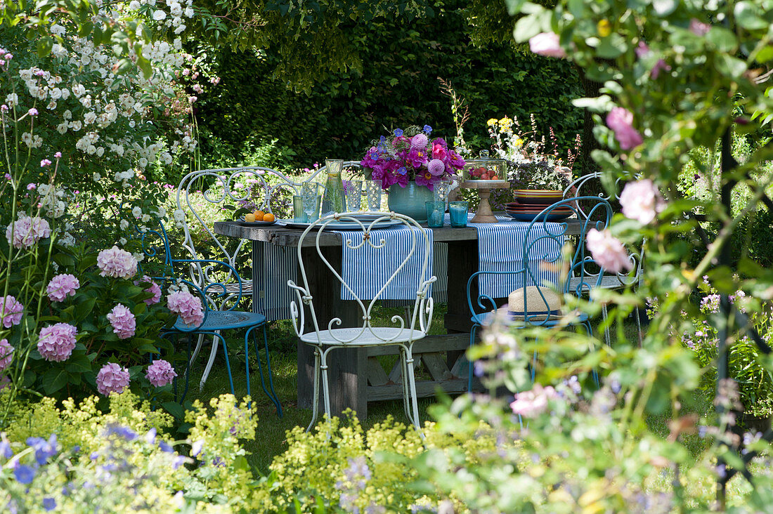 Gedeckter Tisch im Garten mit Strauß aus Pfingstrosen, Rosen und Dahlien