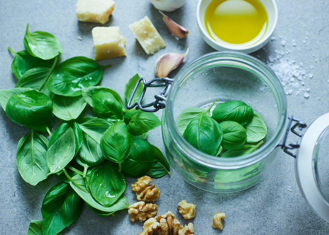 A glass jar with basil and ingredients for pesto