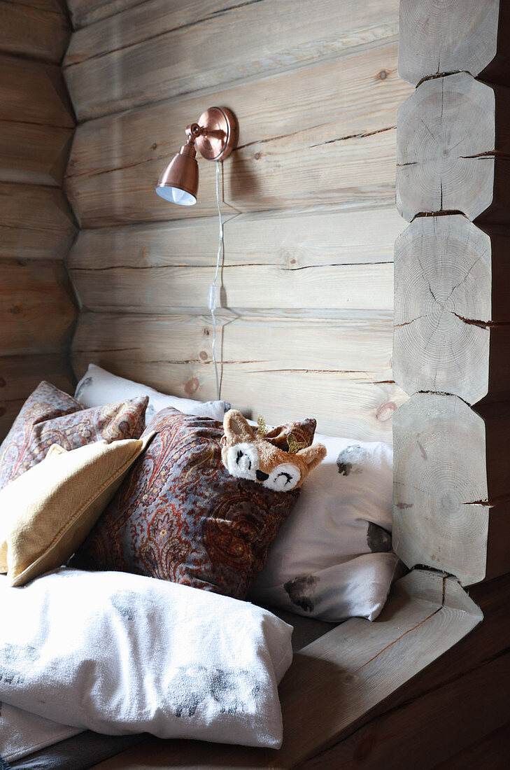 Furry sleeping mask and scatter cushions in cubby bed in log cabin