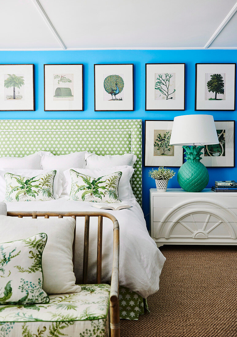 Picture gallery with natural motifs on a bright blue wall above a double bed