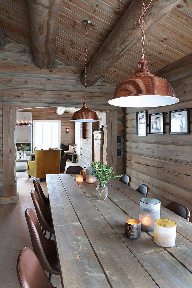 Copper-coloured lampshades above rustic dining table in log cabin
