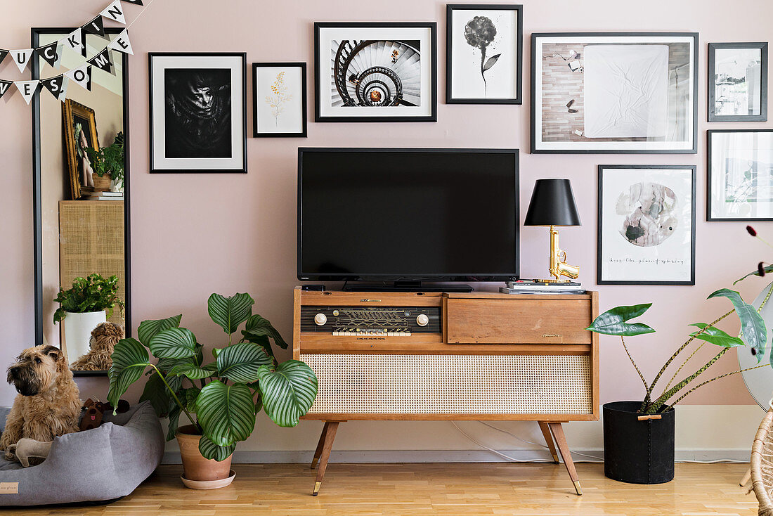 Fernseher auf einem Retroradio vor rosafarbener Bilderwand