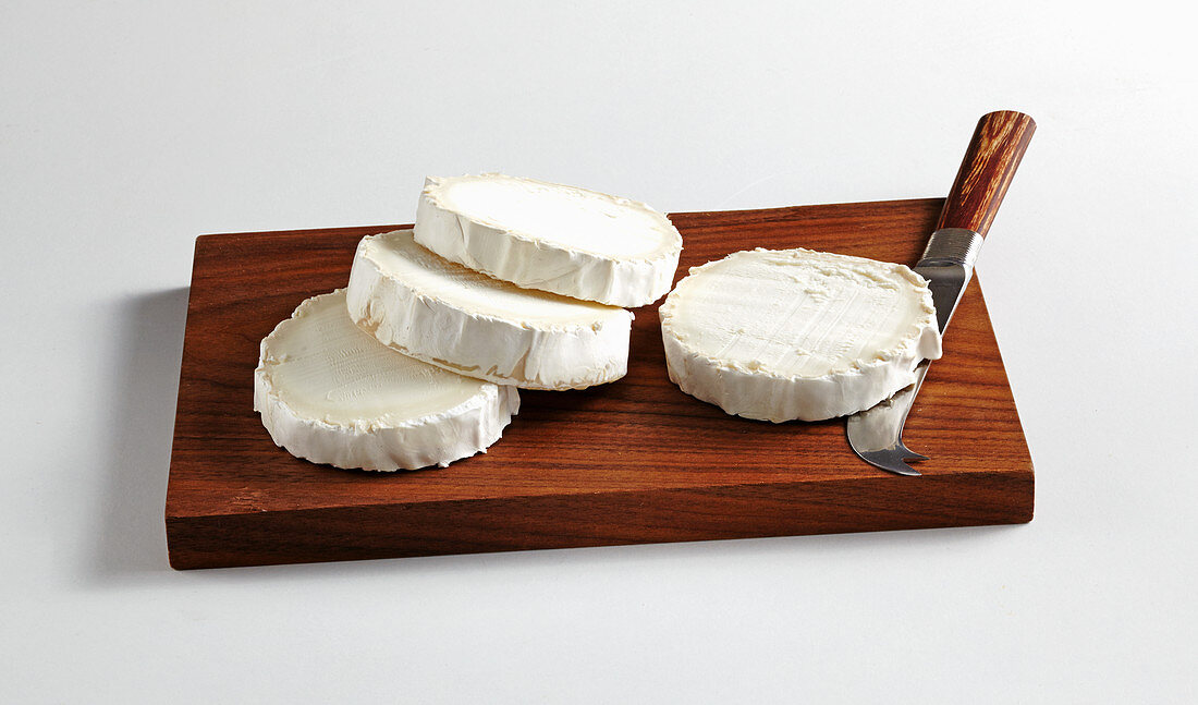 Sliced round goat's cheese with a cheese knife on a kitchen board