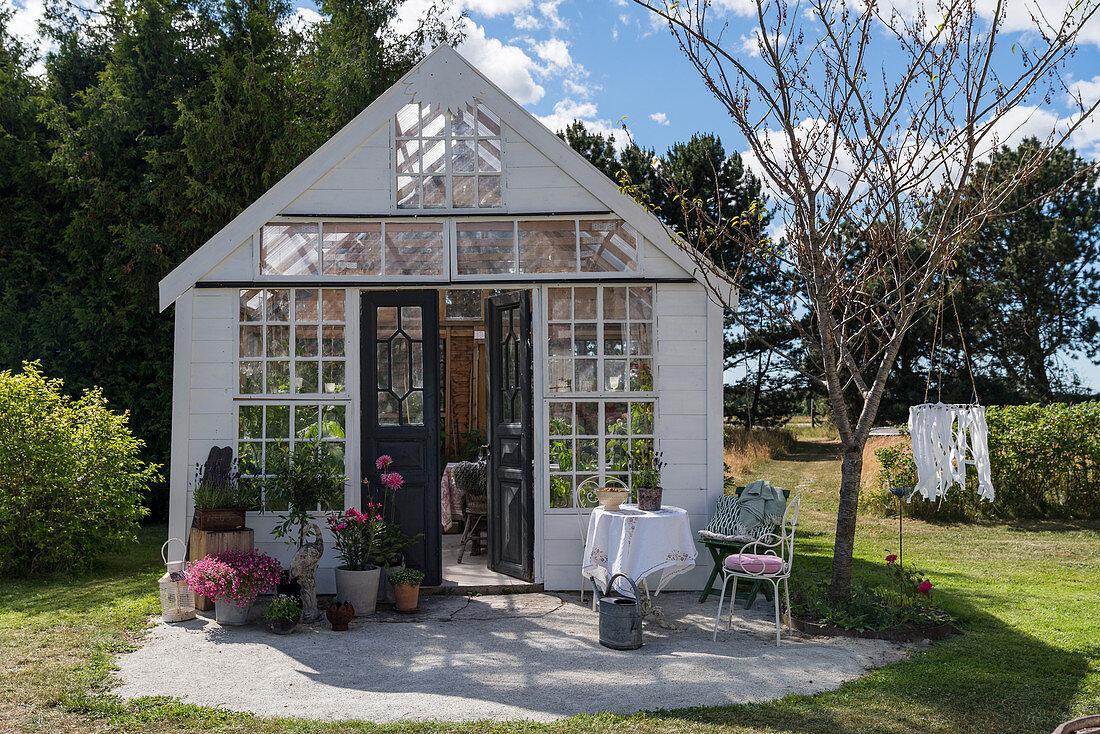 Romantisches Gartenhaus aus alten Fenstern im sommerlichen Garten