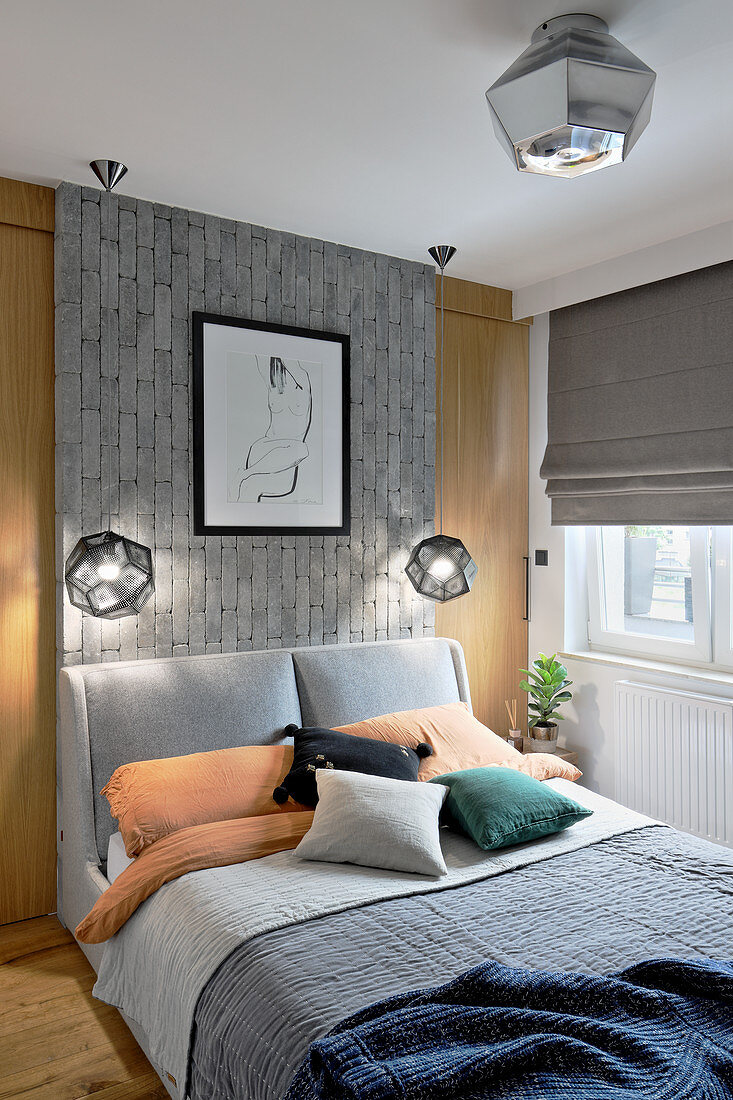 Double bed with grey headboard against grey brick panel in bedroom