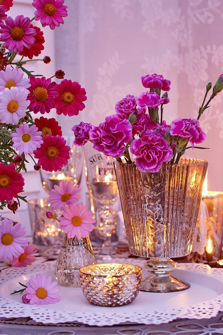Romantic arrangement of carnations, ox-eye daisies and tealights on table