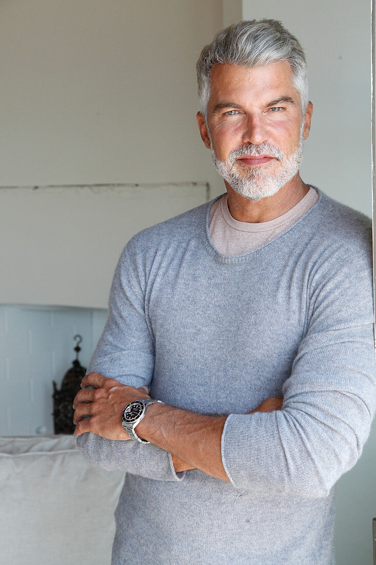 A grey-haired man wearing a light-grey jumper over an under shirt