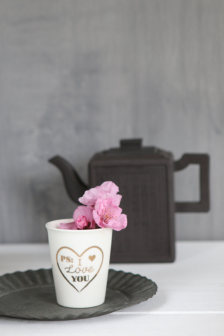 Pappbecher mit goldenem Liebesgruß und rosa Blüten