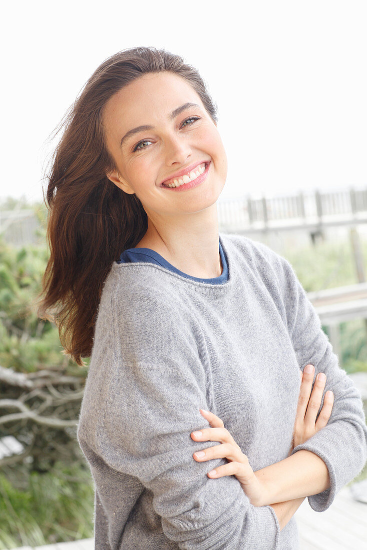 A young brunette woman wearing a grey woollen jumper with an under shirt