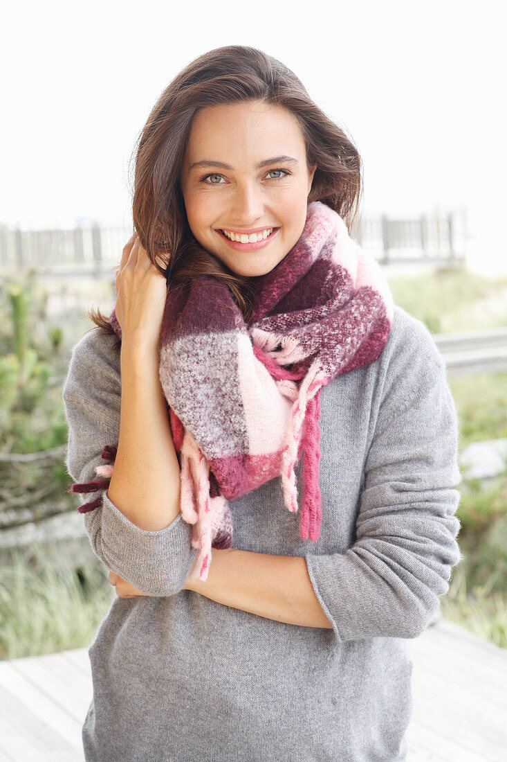 A young brunette woman wearing a grey woollen jumper and a thick scarf