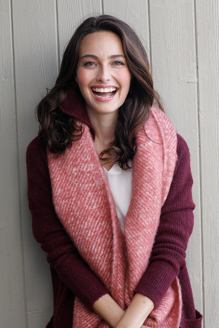 A young brunette woman wearing a wine-red cardigan with a salmon pink woollen shawl