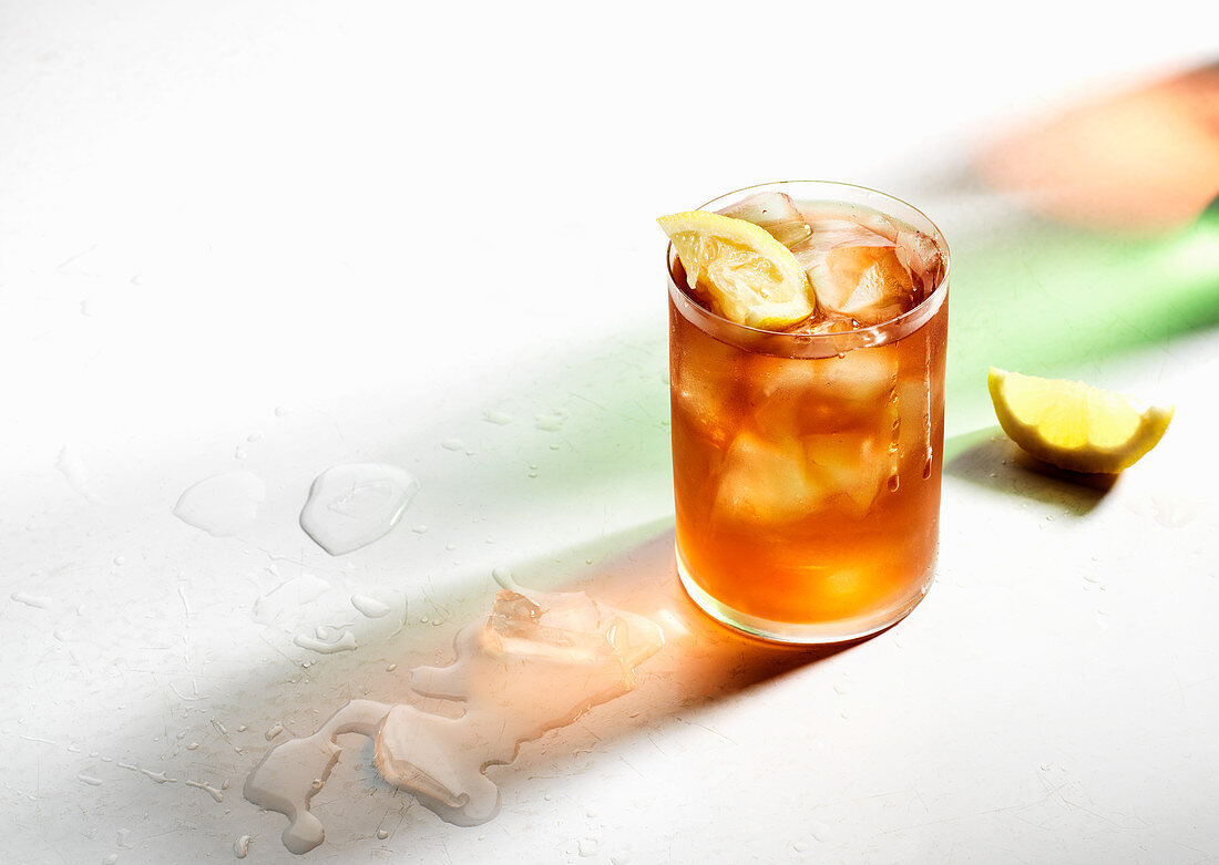 Ice cold iced tea with lemon wedges, drips on glass, colored shadows and melted ice