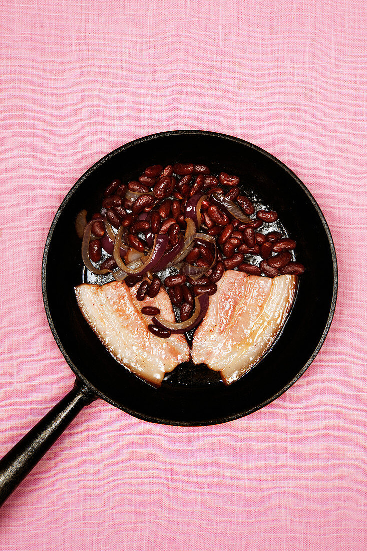 Schweinebauch mit Kidneybohnen und Zwiebeln in Bratpfanne