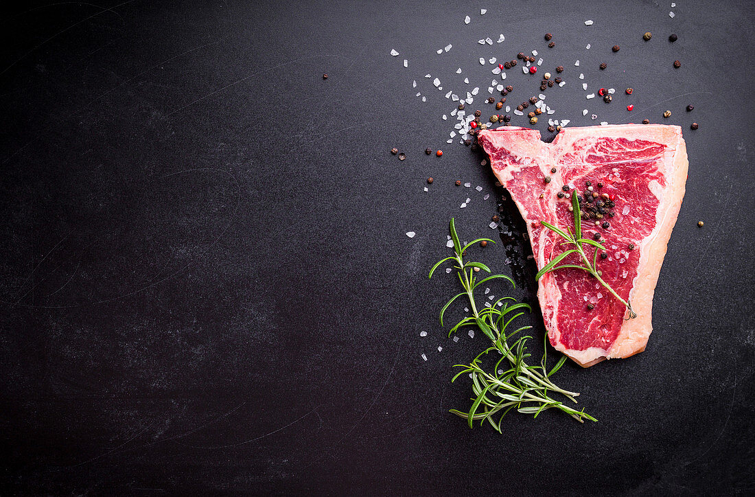 Raw marbled meat steak with seasonings on black chalkboard background