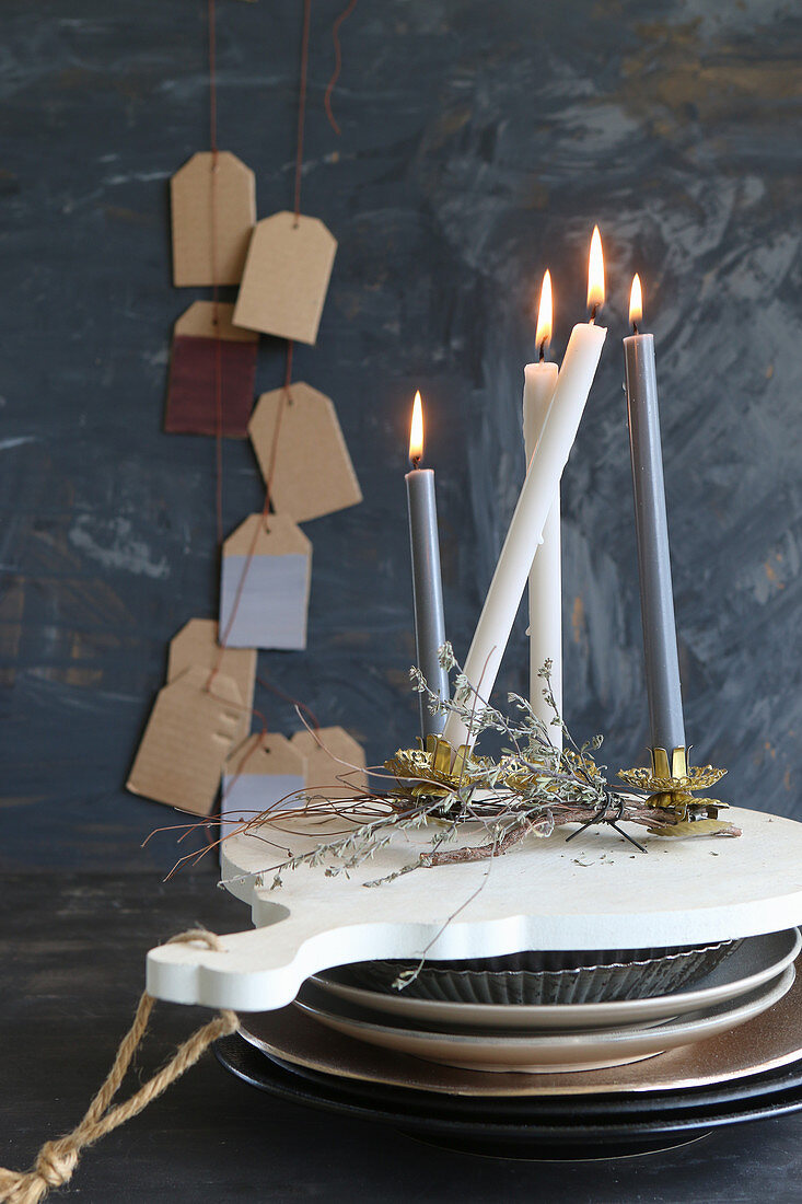 Lot candles on stacked crockery in front of gift tags on wall
