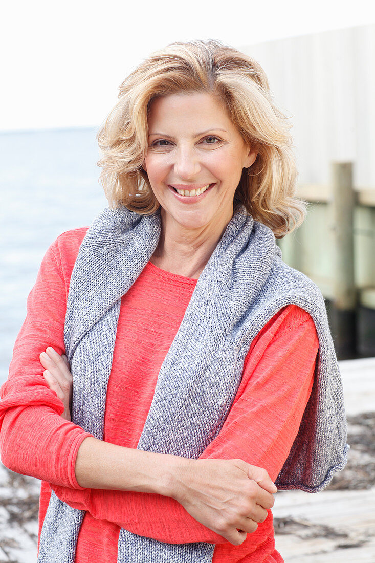 A blonde woman wearing a red long-sleeved top with a jumper over her shoulders