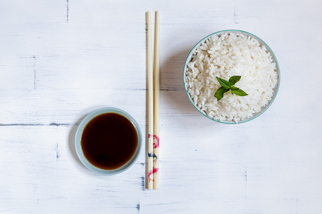 Cooked jasmine rice in a bowl with chopsticks and soy sauce
