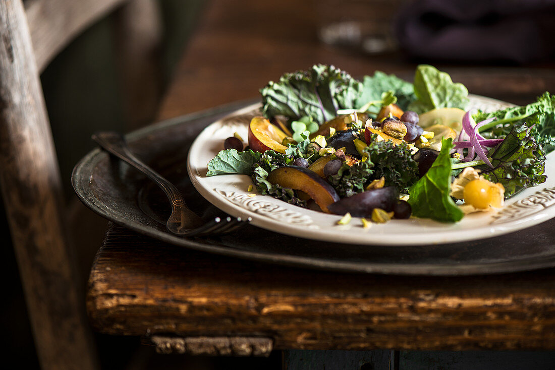 Kale, plum, pistachio salad with onions and ground cherries in rustic farm environment