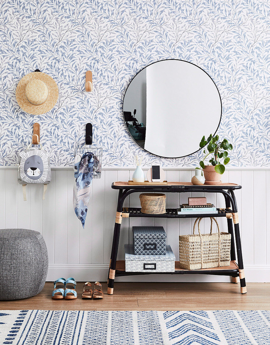 Storage idea in the hallway: table, round mirror above and wall hooks on blue and white wallpaper