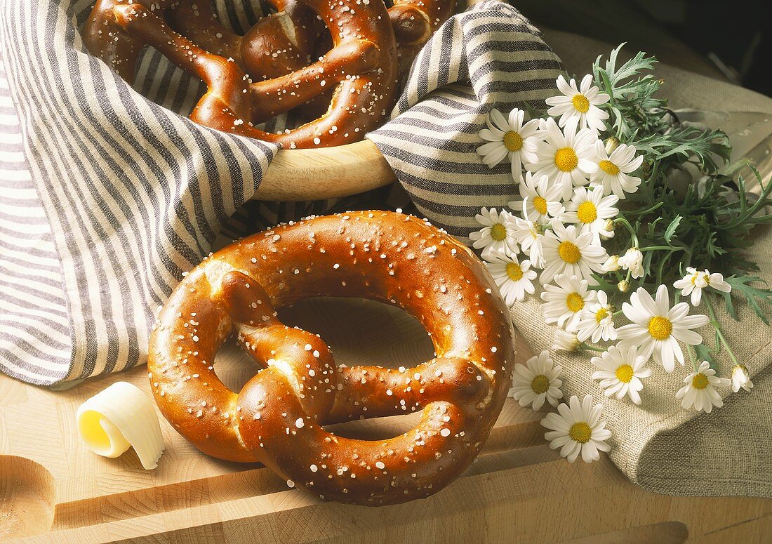 Salt pretzels on wooden board & in bread basket; marguerites