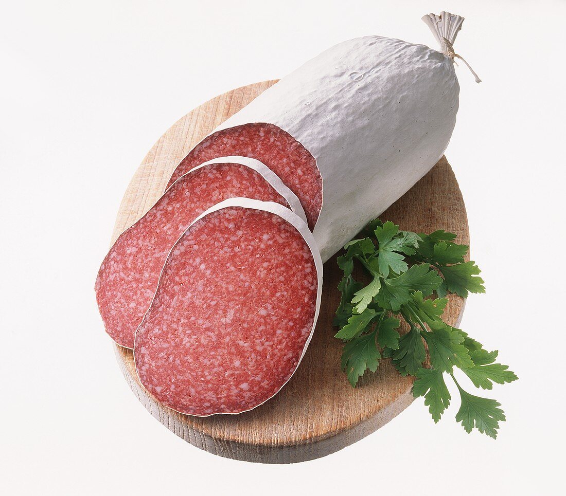 Salami, zwei Scheiben abgeschnitten, mit Petersilie auf Brett