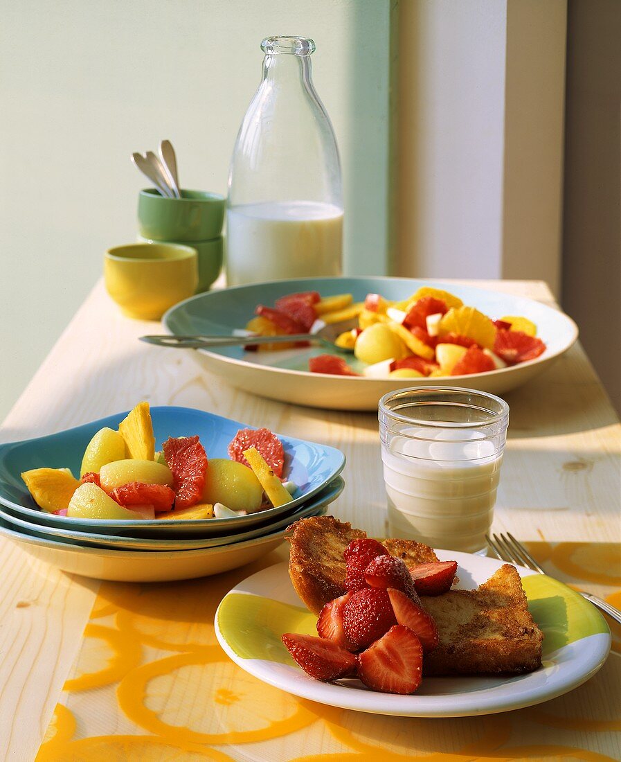 French Toast mit Erdbeeren, Obstsalat & Glas Milch auf Tisch